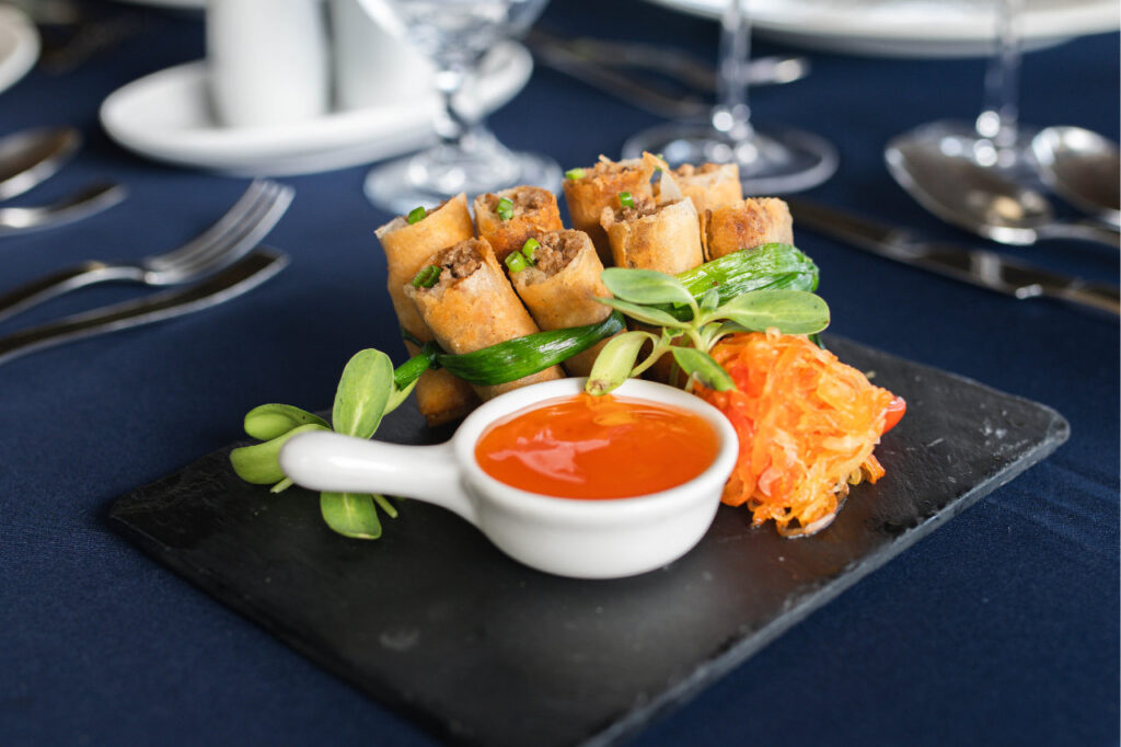 A plated serving of Filipino lumpia spring rolls with sweet chili sauce and fresh garnish at Atmosphere Resorts & Spa.