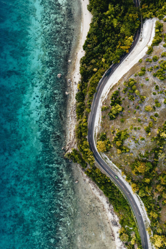 Aerial view of Siquijor’s winding coastal road beside clear turquoise waters and lush tropical greenery.