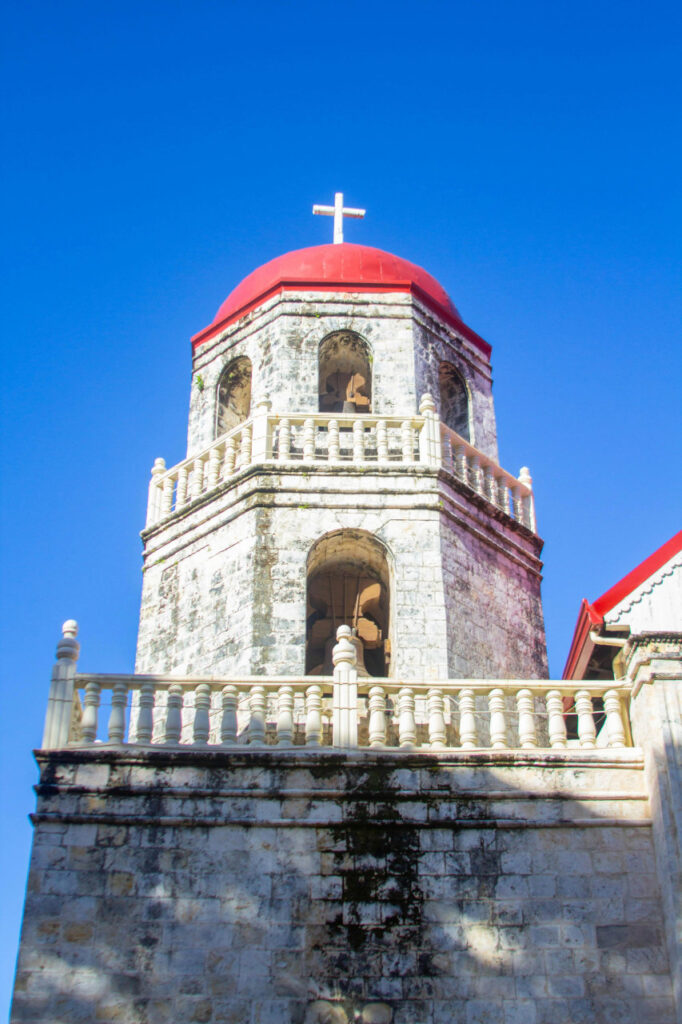 The Bell Tower at the Convent and Mother Grotto in Siquijor, featuring a stone structure with a red dome and a white cross under a bright blue sky.