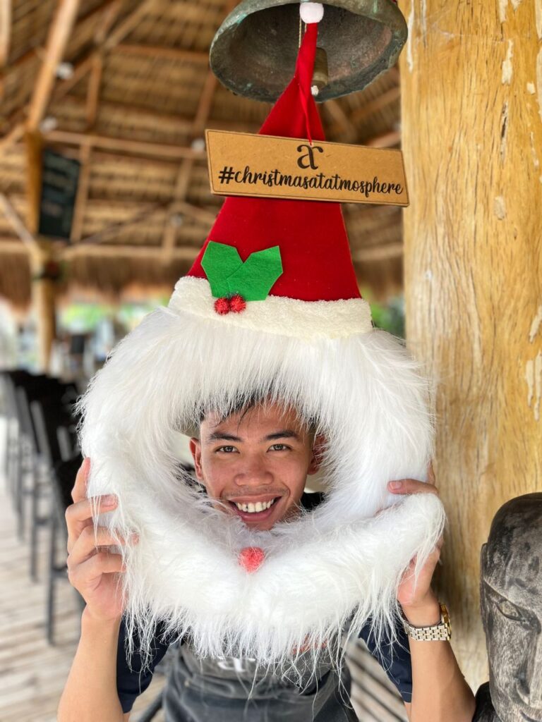 Atmosphere Resorts & Spa staff member smiling and wearing a festive Santa hat decoration during the Christmas season.