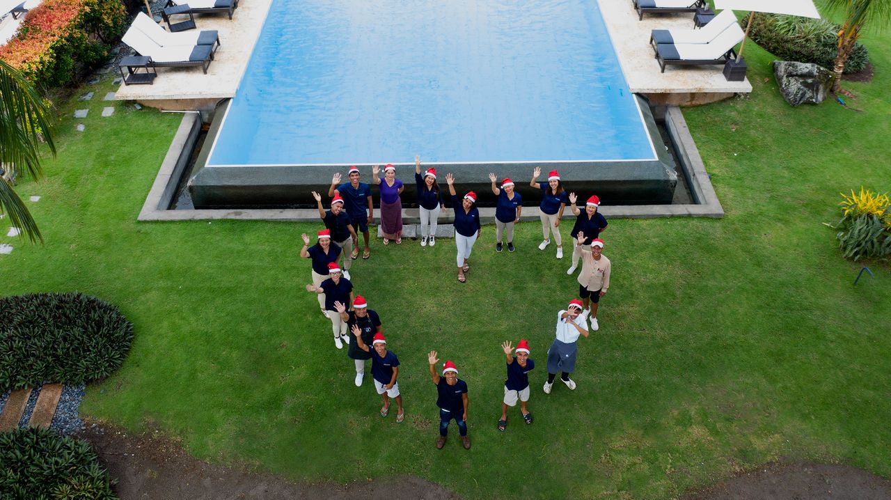 Atmosphere Resorts & Spa team wearing Santa hats, waving beside the resort pool during the Christmas season in Dauin, Philippines.