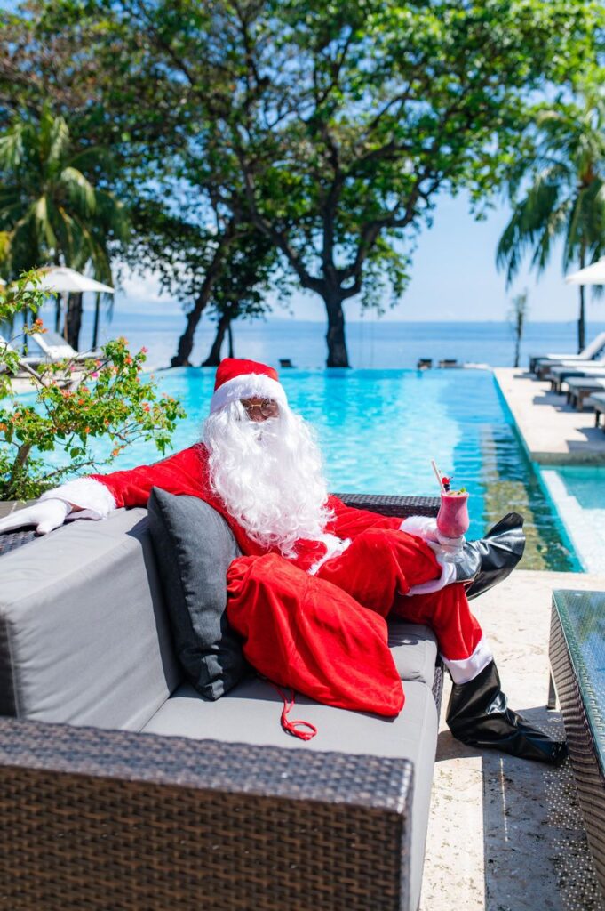 Santa Claus relaxing by the infinity pool at Atmosphere Resorts & Spa, enjoying a tropical Christmas by the sea.