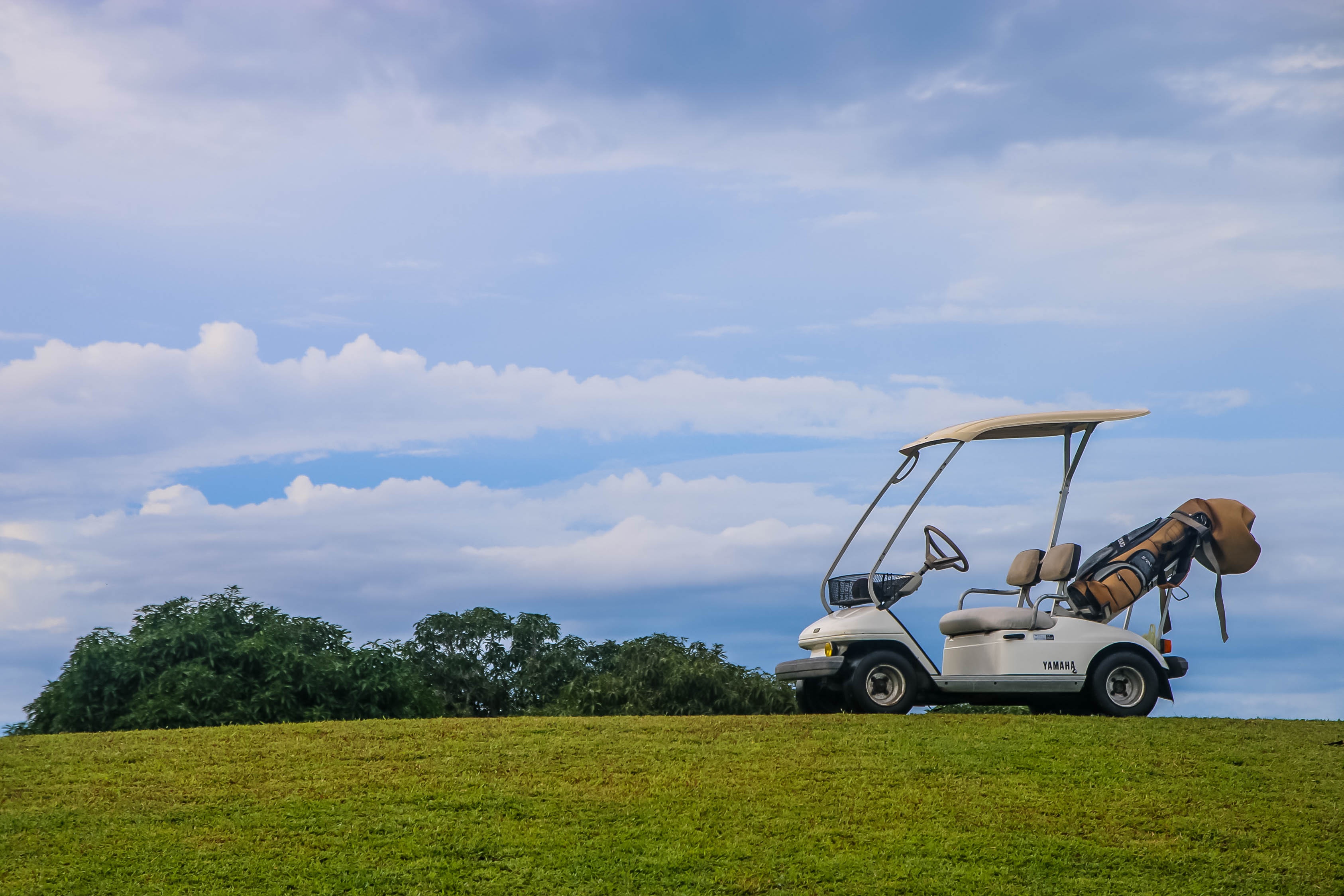 Golf cart parked on a grassy hill at Bravo Golf Course in Negros Oriental under a blue sky.