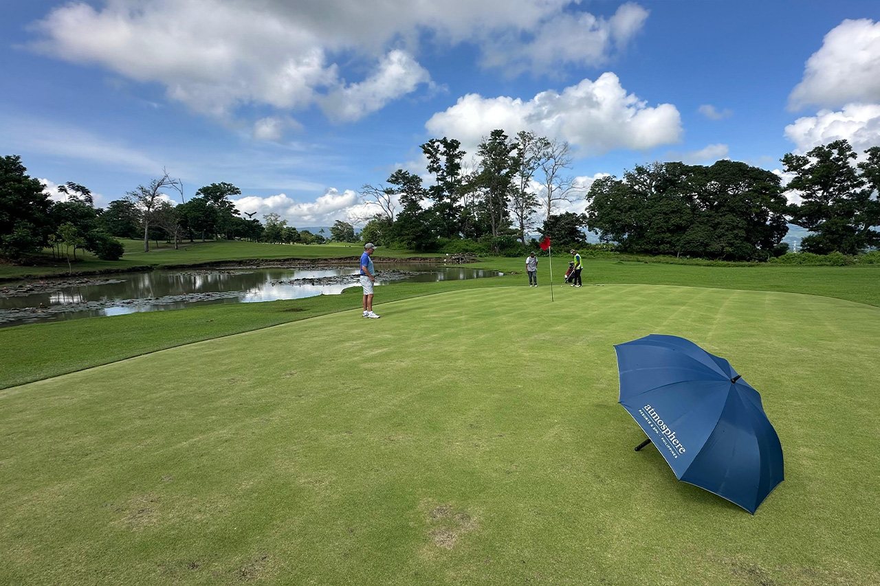 Golfers on the putting green at Negros International Golf & Country Club with water features and open fairways in the background.