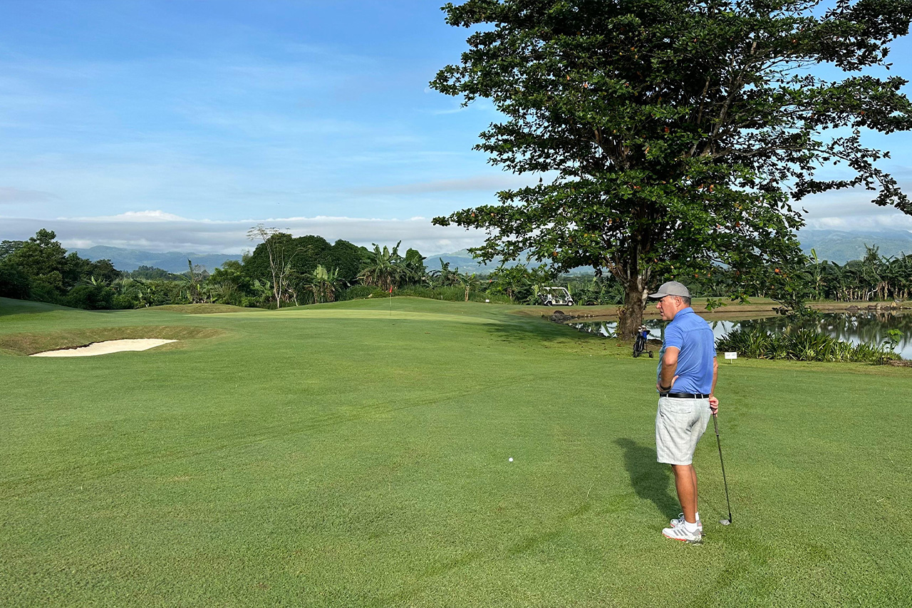 Guest golfer standing on the fairway at Negros International Golf & Country Club with tropical landscapes and water features nearby.