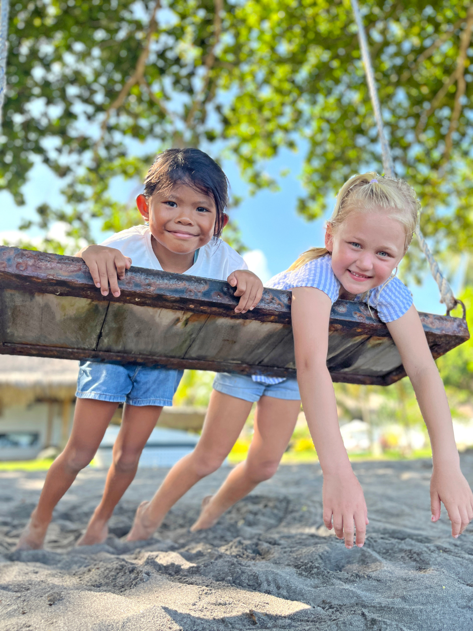 Two children playing on a swing by the beach at Atmosphere Resorts & Spa in Dauin
