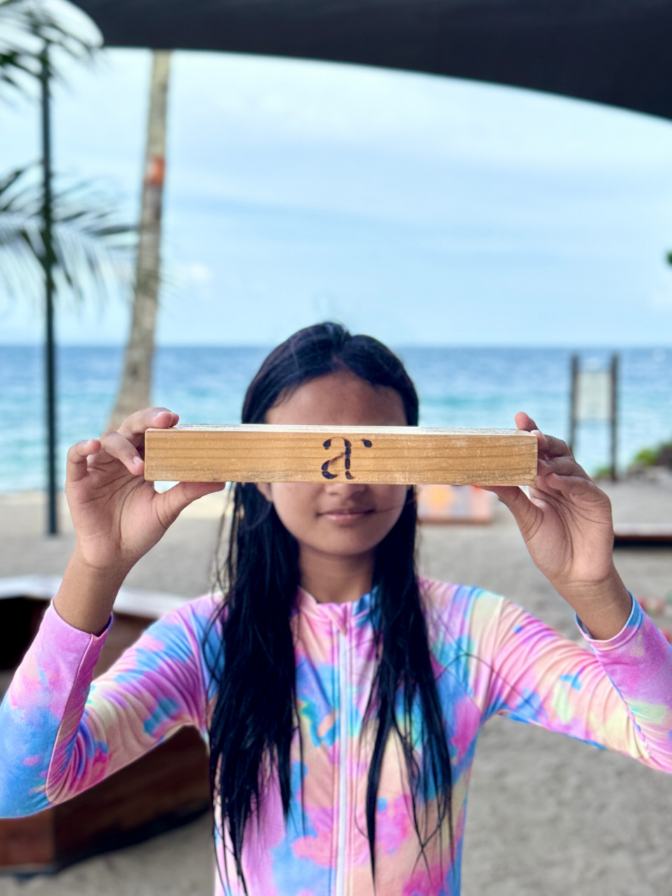 Young girl holding a wooden Jenga block with Atmosphere logo at the beach play area in Dauin