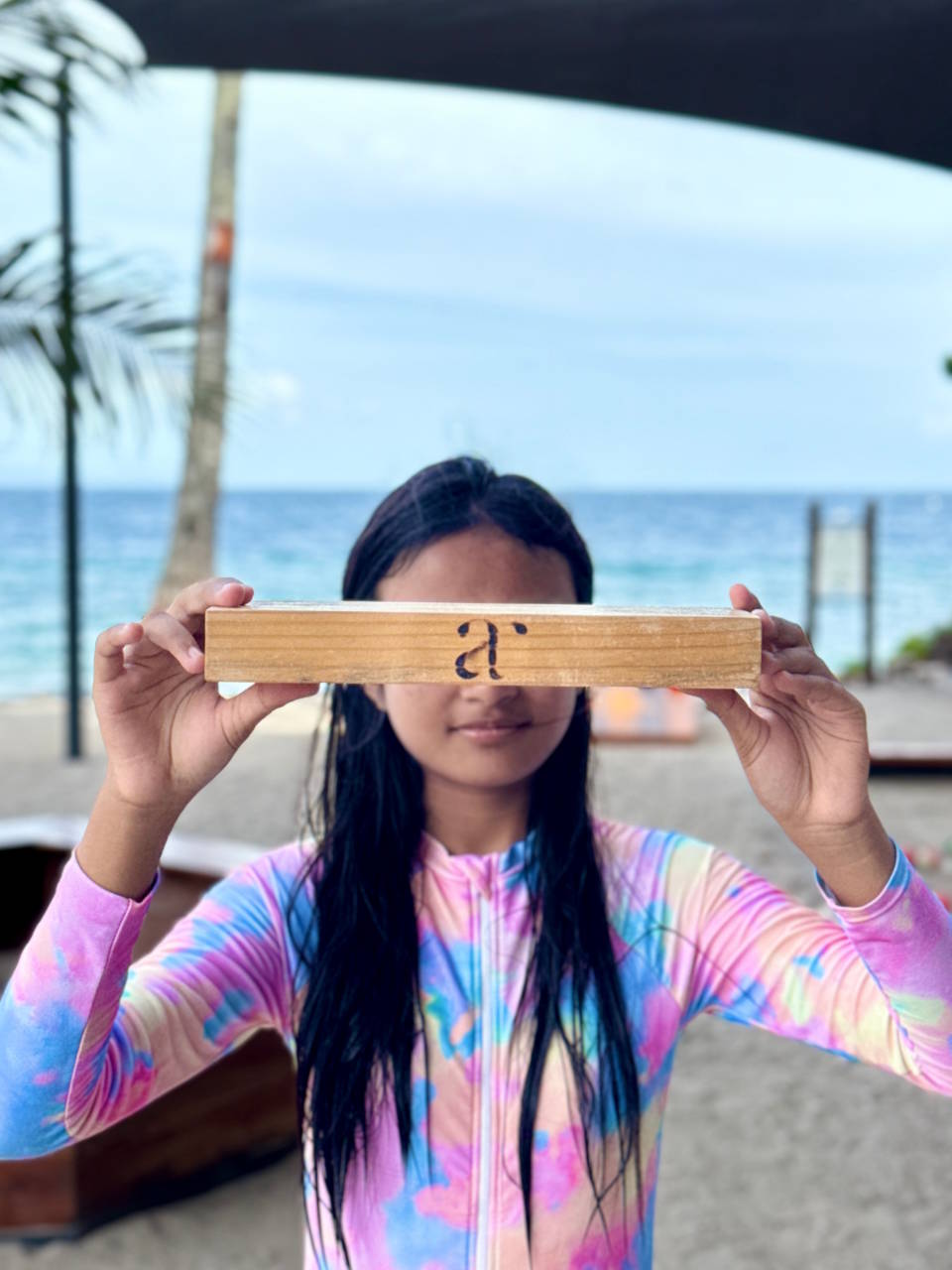 Young girl holding a wooden Jenga block with Atmosphere logo at the beach play area in Dauin