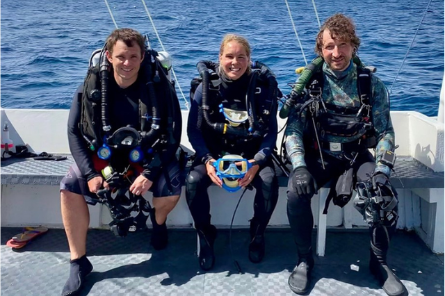 Three members of the BBC underwater filming team sit aboard a dive boat in technical diving gear during filming preparations in Dauin.