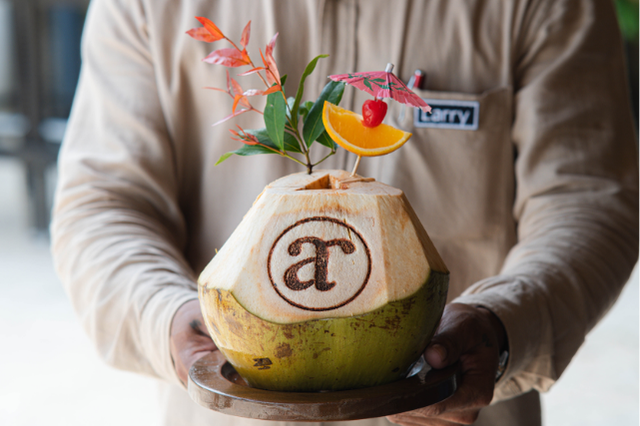 A freshly opened young coconut served at Atmosphere Resorts & Spa, garnished with tropical decorations and presented by a resort staff member.