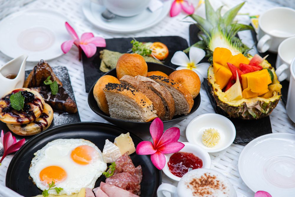 A breakfast spread at Atmosphere Resorts & Spa featuring farm-fresh eggs, homemade breads, tropical fruits, pastries, cheeses, and locally sourced ingredients.