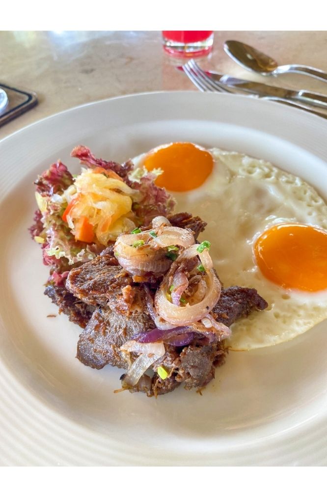 A traditional Filipino beef tapa breakfast served with sunny-side-up eggs and pickled vegetables at Atmosphere Resorts & Spa.