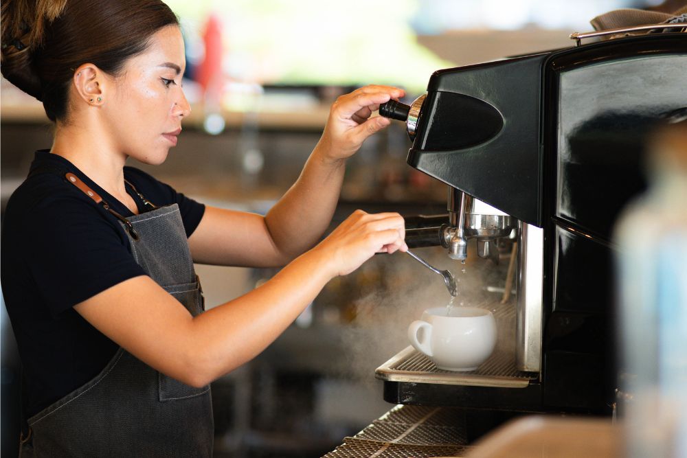 A member of the Atmosphere Resorts & Spa team prepares a freshly brewed cup of coffee using an espresso machine during breakfast service.