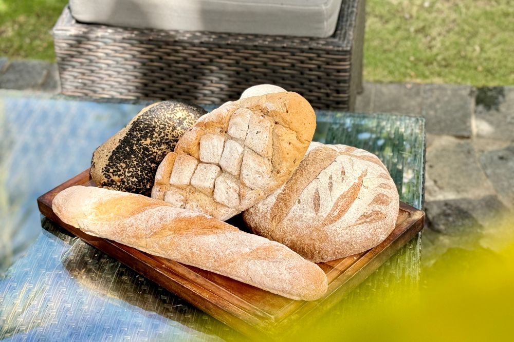 A selection of freshly baked artisan breads, including sourdough, baguettes, and seeded loaves, prepared in-house at Atmosphere Resorts & Spa.