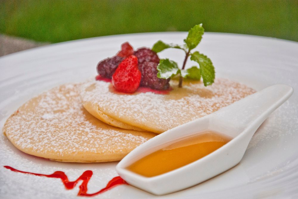 A stack of fluffy pancakes dusted with powdered sugar, topped with berries and fresh mint, served with syrup at Atmosphere Resorts & Spa.