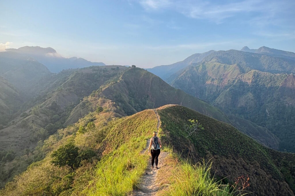 Hiker walking along the ridgeline of Najandig Peak with panoramic mountain and ocean views in Negros Oriental, Philippines.