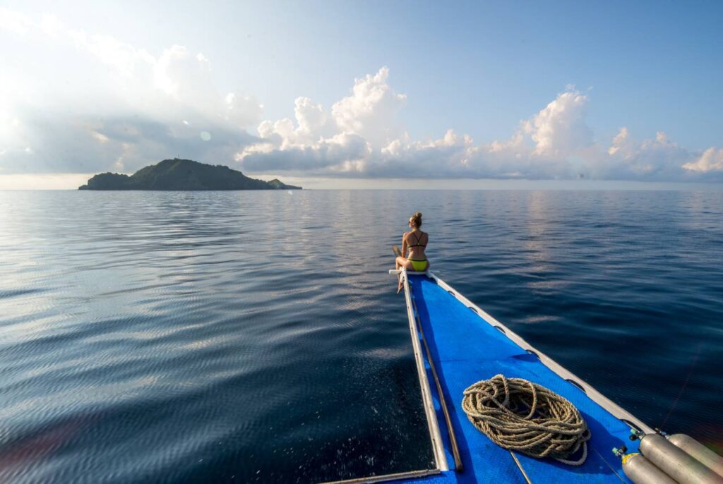 Guest sitting at the bow of a dive boat approaching Apo Island in calm morning waters near Dauin, Negros Oriental. Photo by @banana.journey.