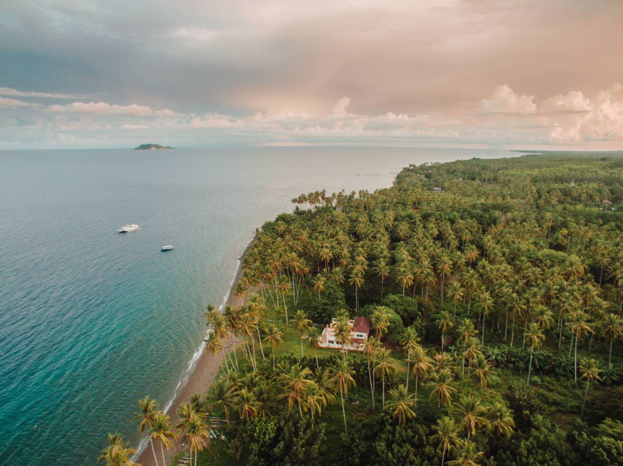 Aerial view of Atmosphere Resorts & Spa on the coastline of Dauin, Negros Oriental, surrounded by lush coconut palms with Apo Island visible in the distance. Photo by @lifeofnois7.