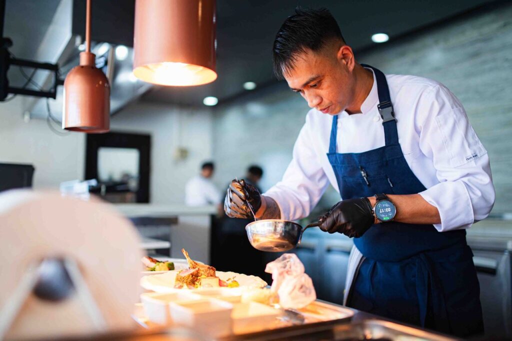 Chef Jun preparing a dish in a professional kitchen at Atmosphere Resorts & Spa