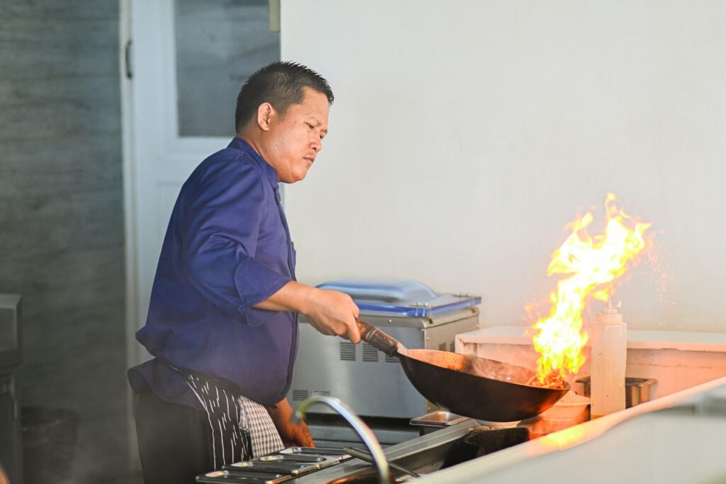 Chef preparing food in a wok over high heat in a professional kitchen