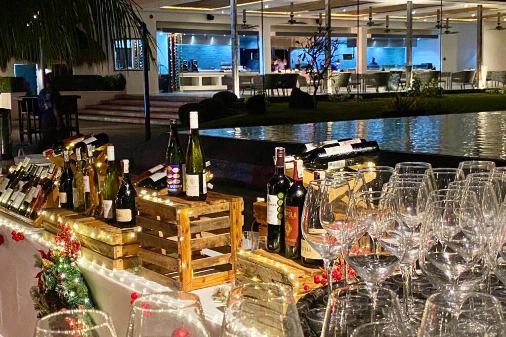 Wine bottles and rows of wine glasses arranged on a Christmas-decorated display beside the pool at Atmosphere Resorts & Spa.