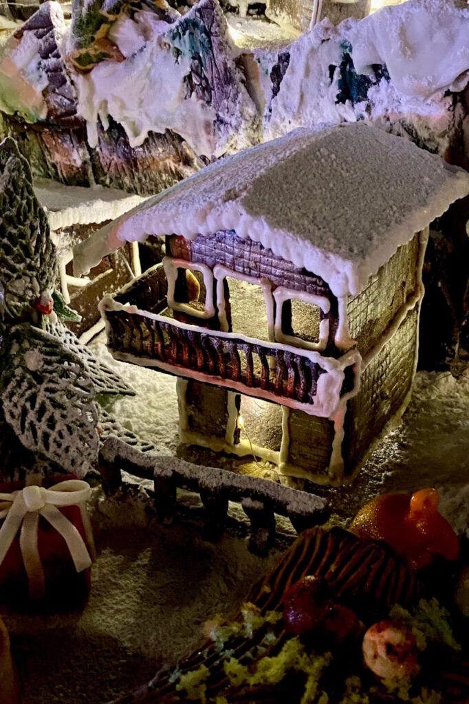 Illuminated gingerbread house with white icing, snowy decorations and festive sweets.