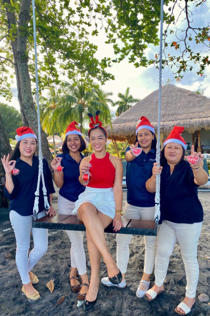 Atmosphere Resorts & Spa team members wearing Santa hats and holding Christmas ornaments while posing together on a garden swing.